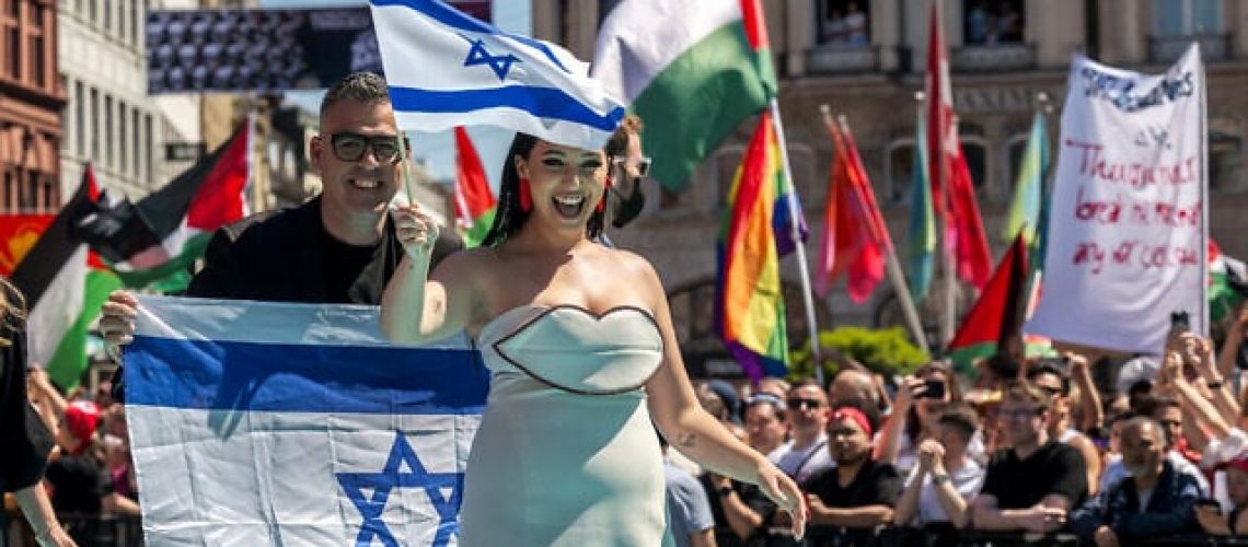 La chanteuse israélienne Yuval Raphael, représentant Israël avec la chanson « New Day Will Rise », marche sur le tapis turquoise à côté de l'hôtel de ville de Bâle, avec les drapeaux palestiniens des manifestants derrière, lors de la cérémonie d'ouverture du concours Eurovision de la chanson 2025 à Bâle le 11 mai 2025. (Fabrice COFFRINI / AFP)